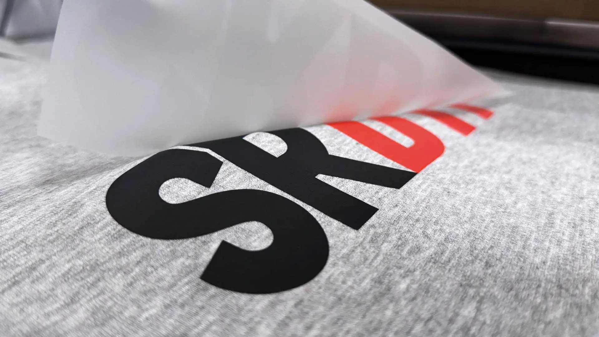 Proceso de estampado DTF textil sobre camiseta gris con diseño en negro y rojo